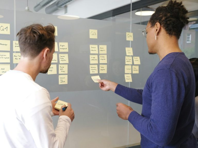 Structured Project Management Two people collaborate, discussing ideas on sticky notes attached to a glass wall.