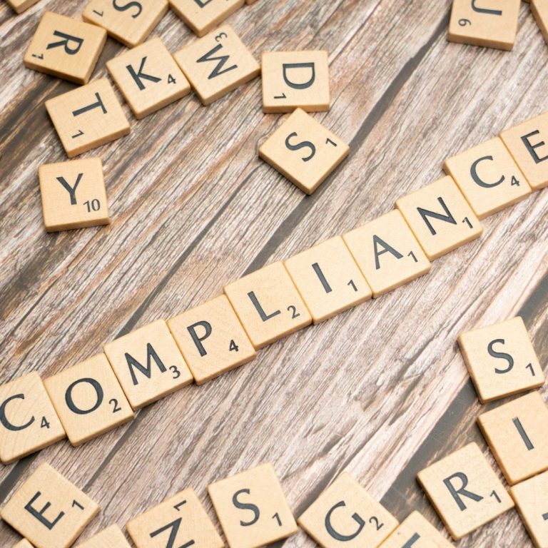 Business and Content Compliance Scrabble tiles spelling the word "COMPLIANCE" on a wooden surface.