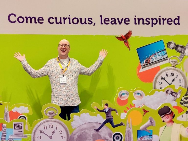Helping Businesses Host Placements Brian, with arms outstretched stands in front of an inspirational backdrop that says "Come curious, leave inspired"